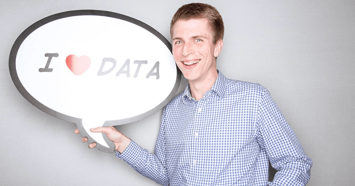 Smiling man in button-down shirt holding an "I <3 data" sign