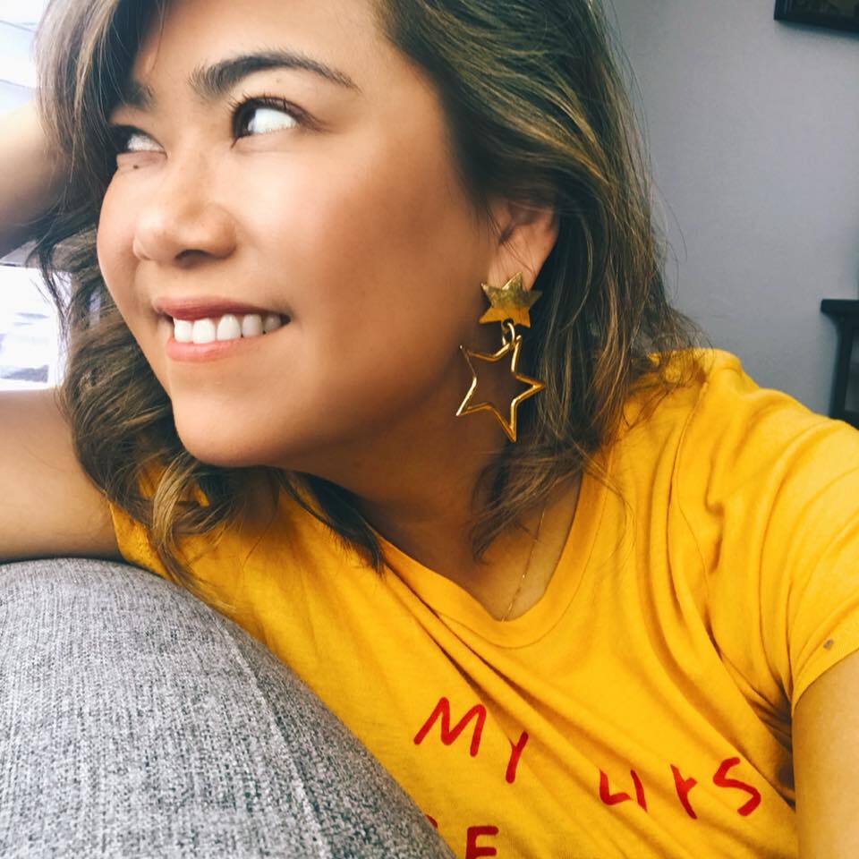 Jo smiling and looking off-camera, wearing a yellow t-shirt and star earrings