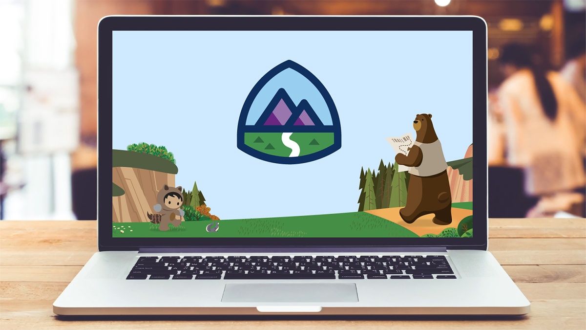 Image of a laptop on a desk with the Trailhead logo (mountains, grass, and a trail)