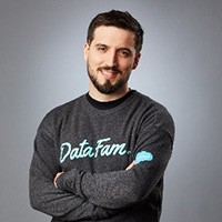Smiling, light-skinned man with dark brown hair, mustache, and beard wearing a gray shirt that says DataFam in light blue