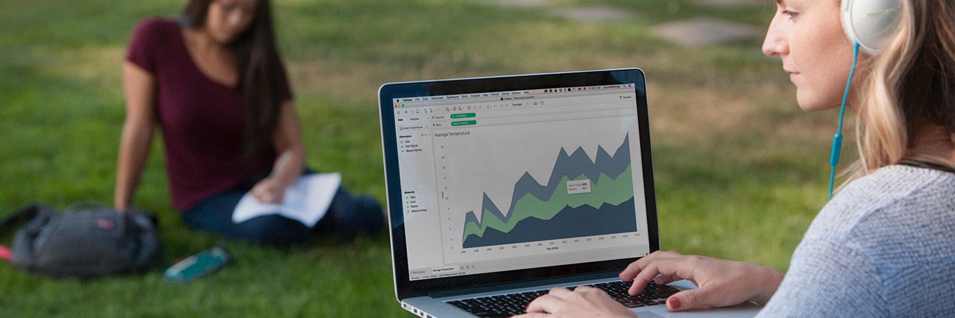 Student working on Tableau on her laptop while sitting in the grass with headphones on