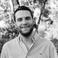 Black and white photo of person smiling in front of a tree