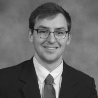 Black and white photo of man in a dark suit and tie, wearing glasses and smiling