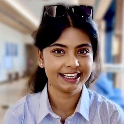 Srishti smiling big at the camera wearing a professional collared light blue shirt and sunglasses on her head.